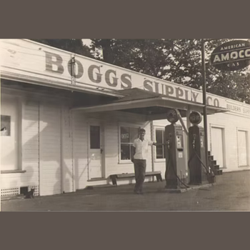 Sepia-toned image of a vintage gas station, "Boggs Supply Co.," with retro gas pumps. A person stands in front, evoking nostalgia and history.