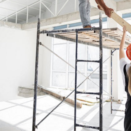 Forklifts, Material Handling & ScaffoldingWorkers in a bright, sunlit room install a plank on scaffolding. One stands on top, another below, wearing a hard hat. The atmosphere is collaborative.